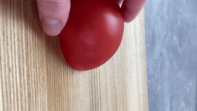 Vertical screen: Close up shot of chef's hands cutting a fresh tomato with knife on wooden board. Cooker preparing vegetarian salad in kitchen, 4k footage