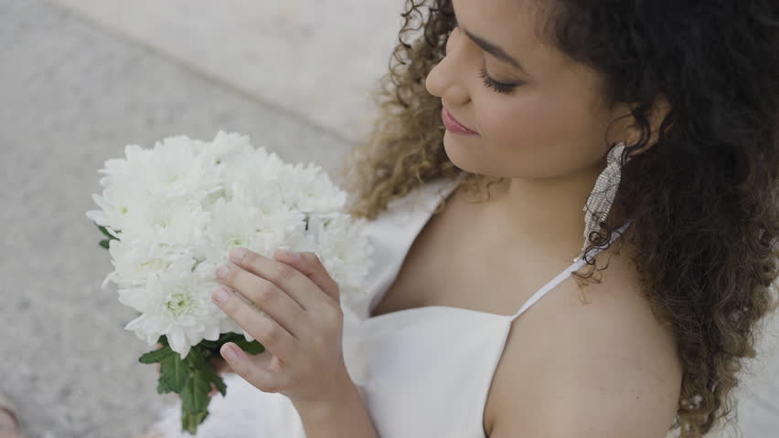 Beautiful young woman with bouquet of white flowers on street. Action. Attractive young woman smiles and holds bouquet of flowers. Smiling woman in dress and bouquet of flowers is waiting for date
