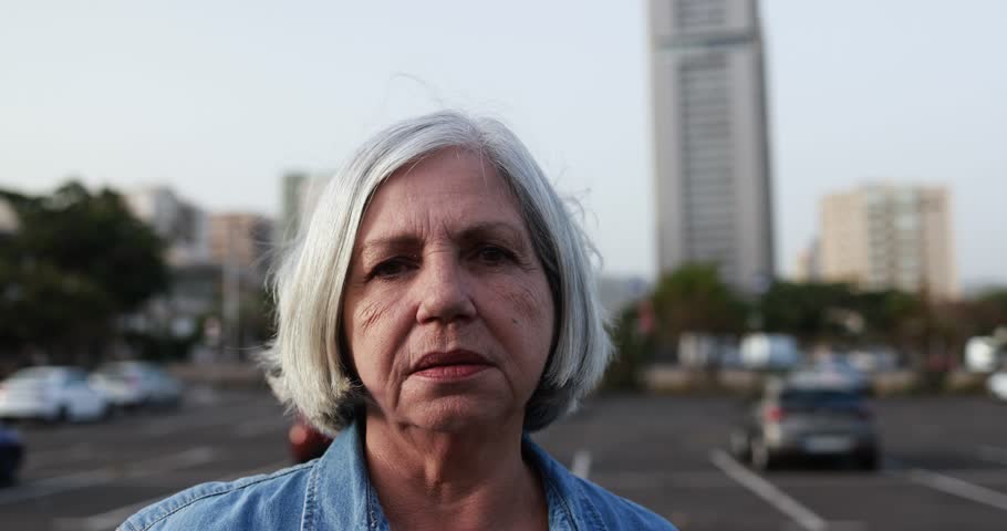 Senior latin woman looking serious on camera with city street in background