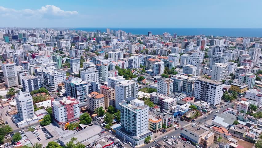 Modern buildings in Santo Domingo town center with sea in background, Dominican Republic. Aerial forward