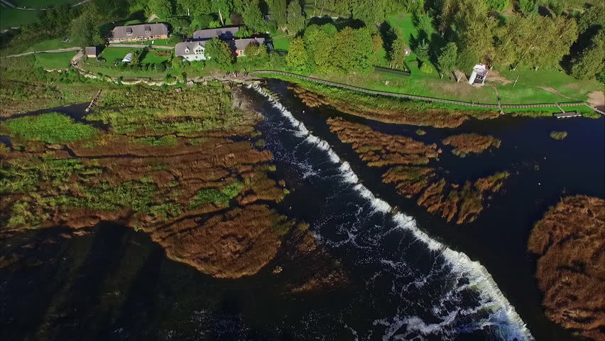 Aerial drone zoom out shot around Venta river rapid waterfall along rural countryside on a sunny day. Rapid located in Kuldiga, Latvia.