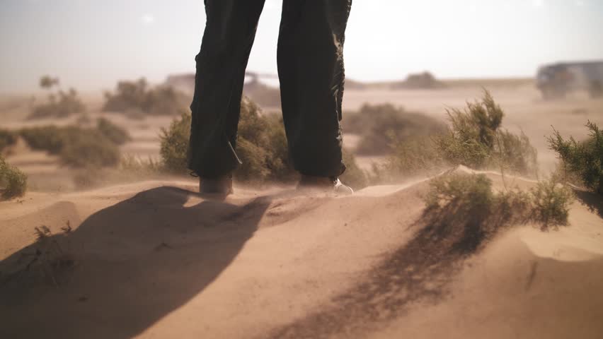 A man in boots stands in the desert, close-up.