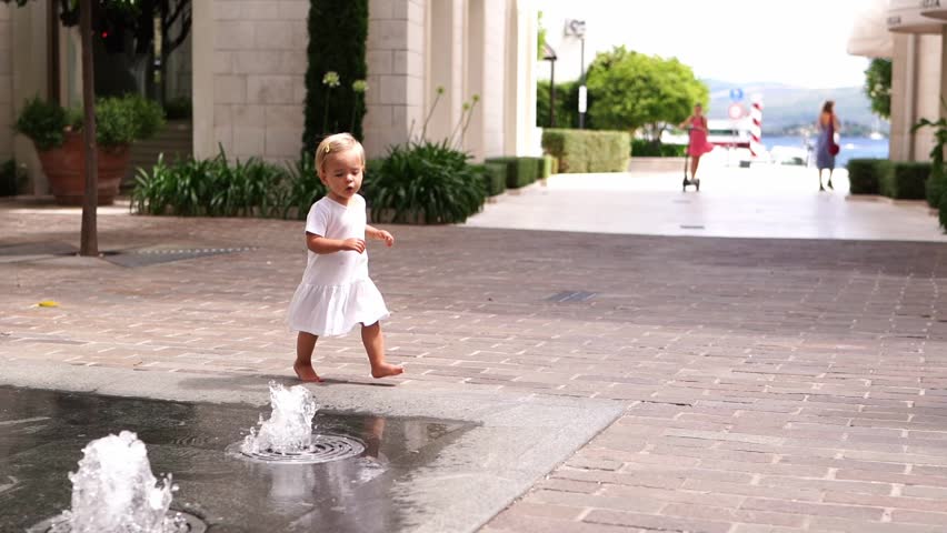 Little girl runs barefoot on the tiles in the courtyard of a building with small fountains