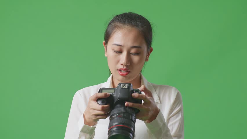 Close Up Of Asian Photographer Looking At The Pictures In The Camera Then Having A Headache While Standing On Green Screen Background In The Studio
