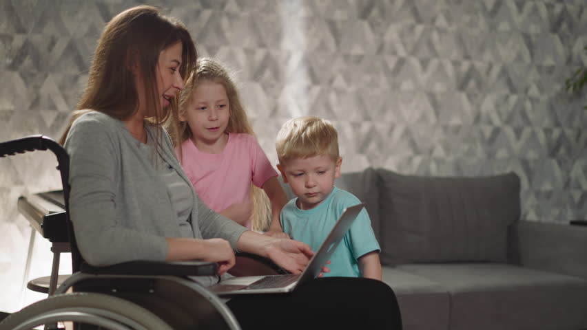 Mother laughs letting children press buttons on modern laptop while working. Caring woman with injury teaches little son and daughter to use gadget