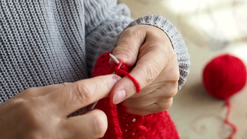 Retired woman knits on knitting needles from red yarn