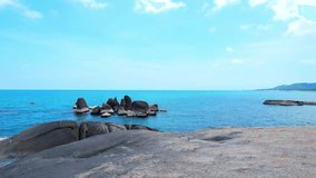 As you walk along the rocky shore, you'll feel the warm sand under your feet and hear the soothing sound of the waves crashing against the rocks. The blue sky above you adds to the picturesque scenery