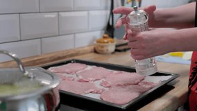 woman salt mill chops pieces of pork on the home kitchen. food preparation process