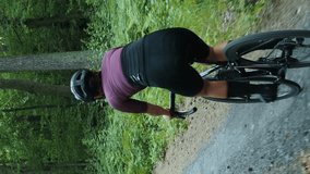 Woman riding bicycle on gravel road in forest. Vertical video. Professional female cyclist training on bicycle outdoors. Sport activity. Healthy lifestyle. Sports training exercises
