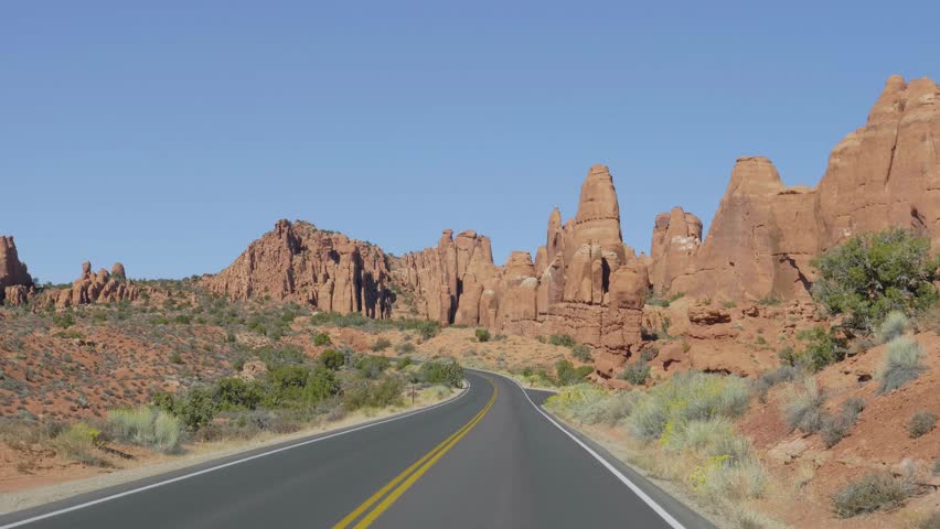 Driving vehicle on empty smooth curved road going into distance to red mountain rocks buttes landscape in dried hot desert Arches national park. Highway with black asphalt and orange road markings