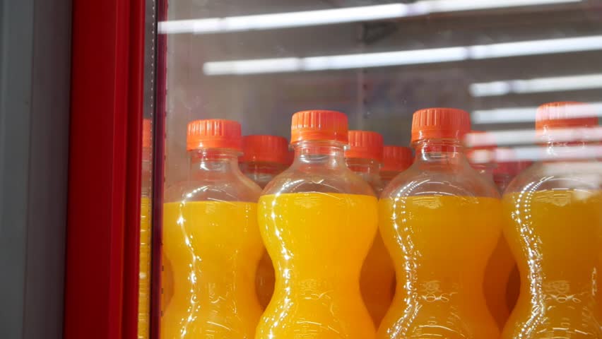 Many orange soda bottles in a store fridge close-up and a male buyer slides the door and takes one Royalty-Free Stock Footage #1102305897