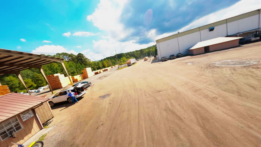 Aerial: Drone Forward Shot Of Truck Carrying Stack Of Lumbers By Warehouse On Sunny Day - Tuscaloosa, Alabama