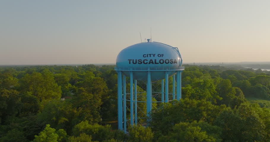 Aerial Panning Shot Of Tall Water Tower Amidst Green Trees, Drone Flying Forward During Sunset - Tuscaloosa, Alabama