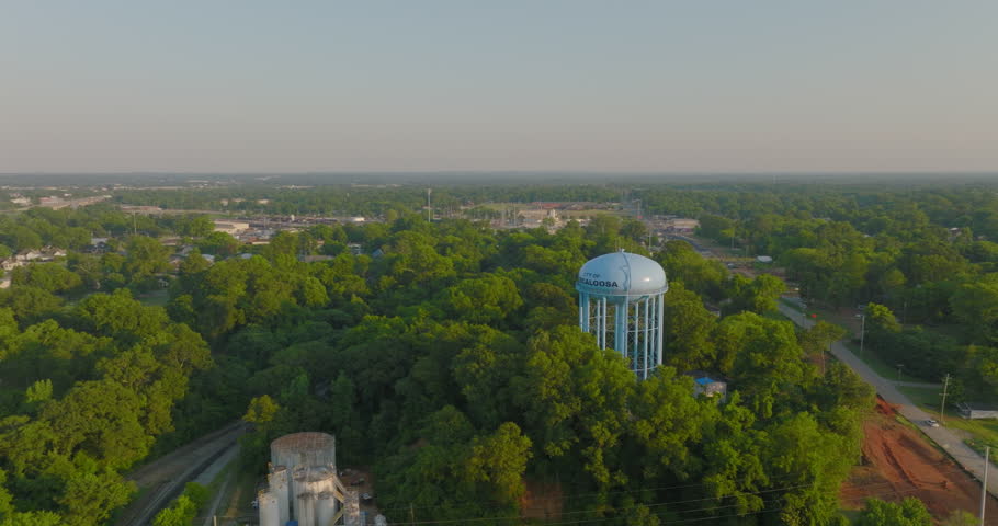 Aerial Panning Shot Of Text On Tall Storage Tank Amidst Green Trees In City Against Clear Sky - Tuscaloosa, Alabama