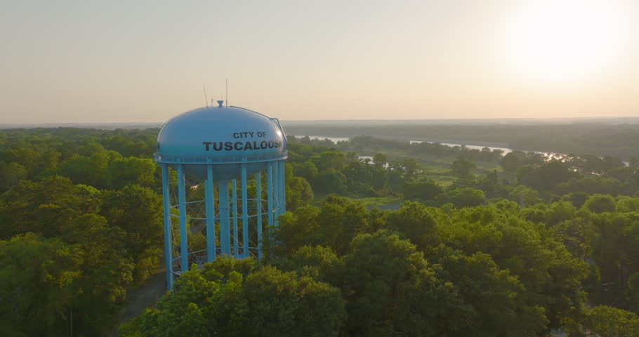 Aerial Panning Shot Of Tall Storage Tank Amidst Green Trees By River During Sunset - Tuscaloosa, Alabama