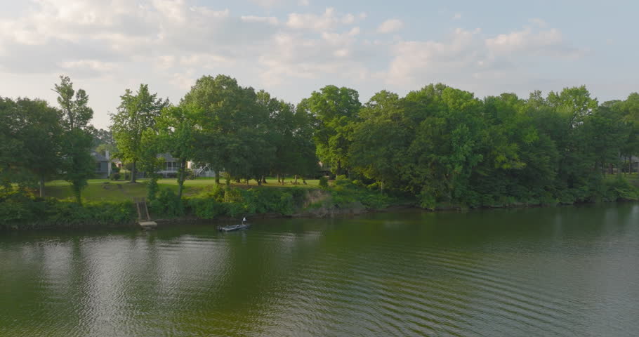 Aerial Forward Shot Of Man Fishing In River By Green Landscape Against Cloudy Sky - Tuscaloosa, Alabama