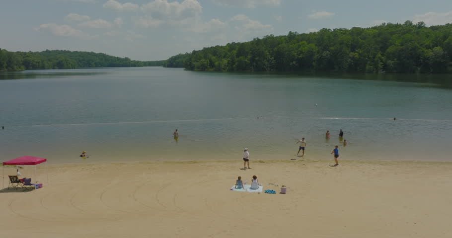 Aerial: Drone Shot Of Friends Playing On Riverside At Beach By Green Forest Trees Against Cloudy Sky - Tuscaloosa, Alabama
