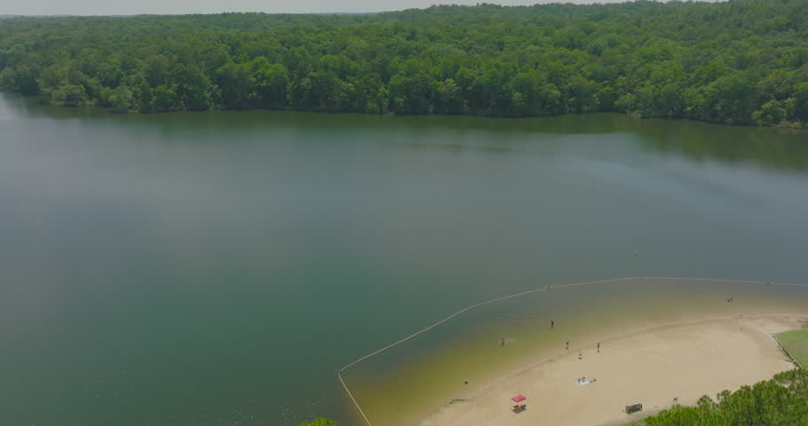 Aerial Shot Of People Playing At Beach On Sunny Day, Drone Flying Backwards Over Green Trees - Tuscaloosa, Alabama