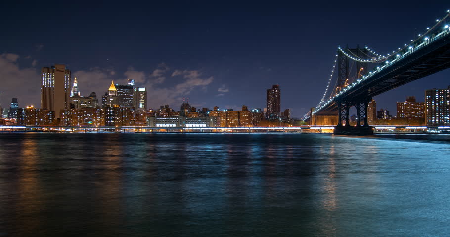 Lockdown Time Lapse Shot Of Brooklyn Bridge Over The East River In Illuminated Downtown City At Night - New York City, New York