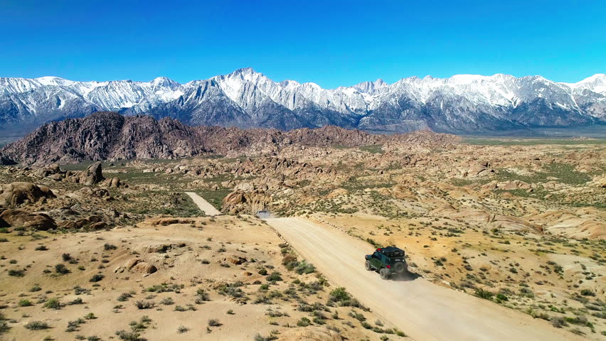 Aerial: Drone Forward Shot Of Adventure Vehicle And Pick Up Truck Moving On Road Towards Snow Covered Mountains Against Clear Sky - Big Pine, California Royalty-Free Stock Footage #1102309159