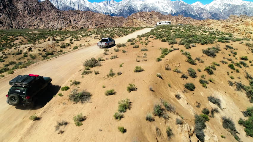 Aerial: Drone Tilt Down Forward Shot Of Pick-Up Truck And Off-Road Vehicle Moving On Road In Desert - Big Pine, California Royalty-Free Stock Footage #1102309161