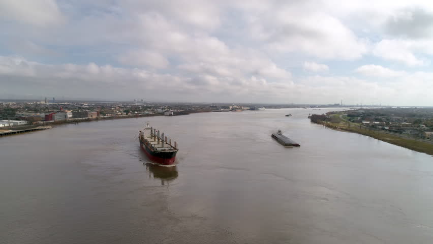 Aerial Panning Shot Of Barge And Bulker Moving On The Mississippi River Amidst Landscapes Under Clouds - New Orleans, Louisiana