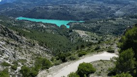 Female cyclist descent on gravel bike,video captured on drone in spanish majestic landscape.Gravel cycling with a mountains and lake view.Cycling in nature on sunny summer day.Guadalest Reservoir