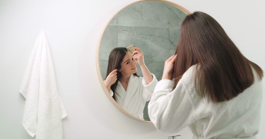 Happy beautiful woman combing her hair in front of mirror. Camera moving right | Shutterstock HD Video #1102312909