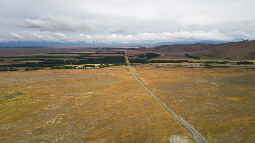 Drone shot of long road in yellow landscape. Cozy downtown of Queenstown in moody cloudy weather, New Zealand. central otago flats during cloudy day