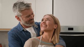 Happy family portrait adult Caucasian couple at home kitchen hugging cuddling smiling to camera toothy cook together. Middle-aged homeowners in love senior man and woman husband and wife smile cooking - Powered by Shutterstock - Get 15% off with code: PIKWIZARD15