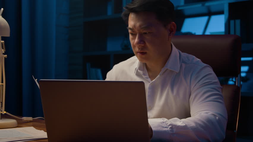 Stressed exhausted pensive thinking Asian mature man businessman at night office late time overworked with business documents depressed worried about financial problem doing paperwork broken computer Royalty-Free Stock Footage #1102316505