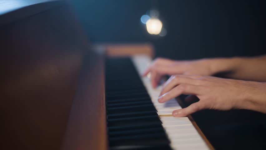 
A close-up of a man playing an old upright piano. Dolly shot. A light bulb is visible in the background. Royalty-Free Stock Footage #1102317361