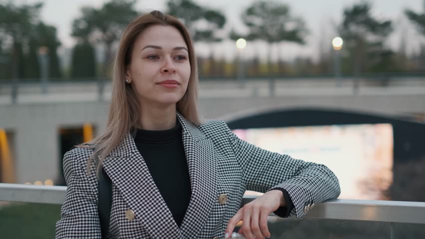 A beautiful slender woman is waiting for someone against the background of a street cinema in the evening