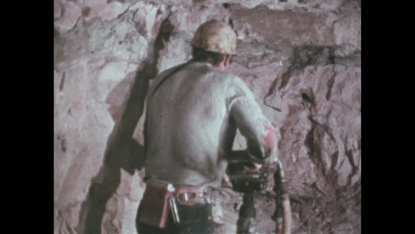 1970s: miner drills as air blows on his shirt from tube, smoke sucked into metal tube, man squeezes device to blow smoke, which dissipates, man in lab with wall of meters inserts tool in plastic box