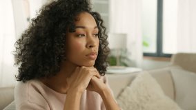 Close up face sad thoughtful young African American single woman looking away thinking of problems. Woman of color siting on sofa alone at modern home troubled with negative thought in slow motion 4K - Powered by Shutterstock - Get 15% off with code: PIKWIZARD15