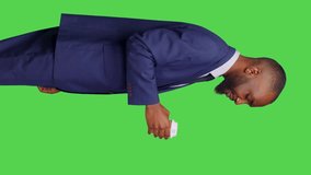 Vertical video: Profile of male office worker enjoying coffee cup in studio, standing over green screen backdrop. Businessman being confident and positive drinking caffeine beverage on camera