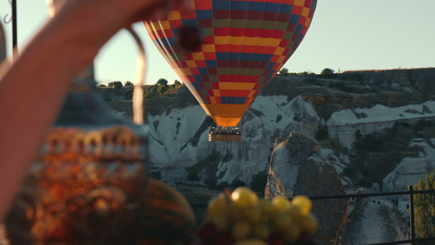 Close-Up of hot air baloon on sunrise in Cappadocia. Forefront young woman picking berries.