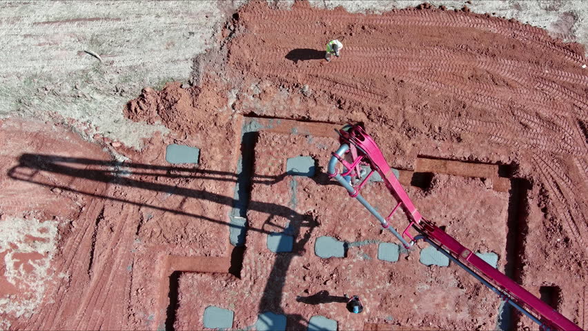 As workers pour concrete for foundation of building using an automatic pump is being directed