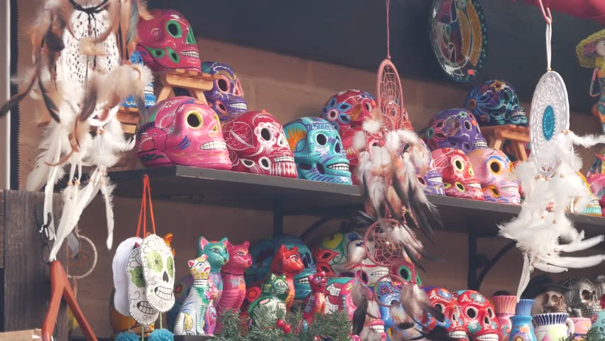 Mexican souvenirs on market stall, colorful painted skulls and dream catchers. Multicolor vivid ethnic ornaments, bazaar or marketplace. Ceramic crafted death symbol for sale on counter. Day of Dead. Royalty-Free Stock Footage #1102338127