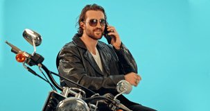 Phone call, man and motorbike in studio on blue background for road trip, freedom and fun with biker aesthetic. Smartphone, conversation and guy driver with motorcycle for vacation, journey or riding