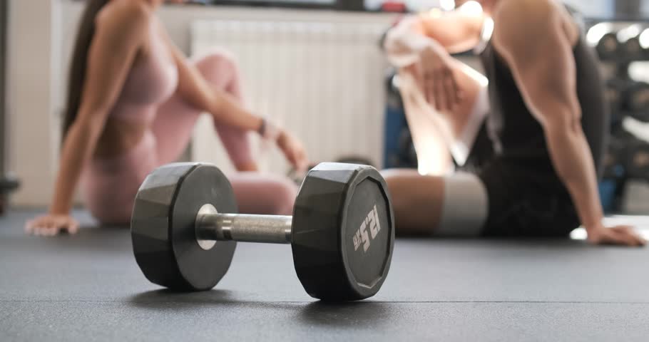 Unrecognizable man and woman talking in gym near dumbbell