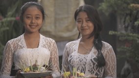 Two Beautiful Balinese Women Girls with Traditional Outfits Smiling Holding Canang Sari Daily Offerings