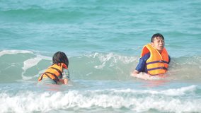 Kid sea beach concept, kids playing sea on beach of slow motion video view on sunny background, happy children wearing life jacket for swimming in sea, slow motion wave of seascape on green water sea
