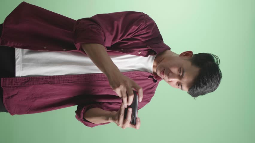 Asian man playing mobile game wins with green screen background.