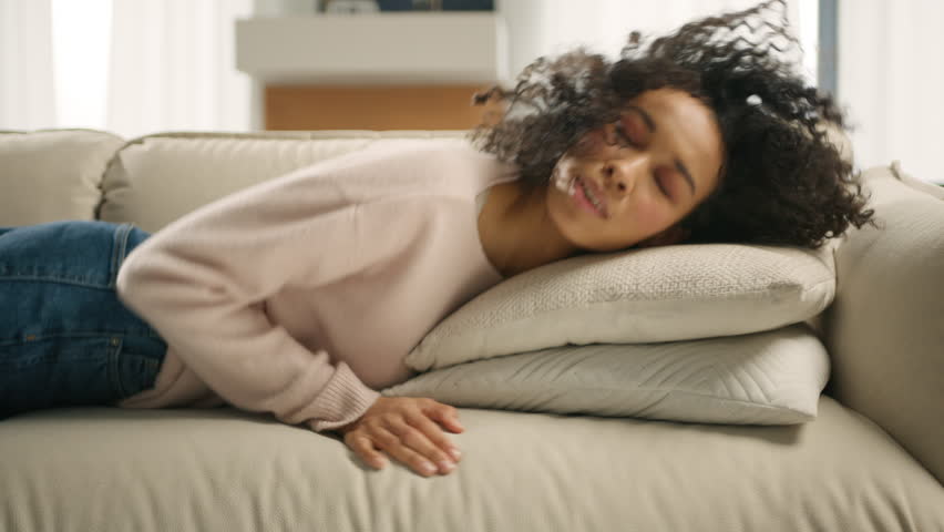 Overloaded exhausted young woman of color in casual sweater came home after work, felt down on sofa, feeling like squeezed lemon. Tired overworked person hard day, lack of energy after party concept  | Shutterstock HD Video #1102369003