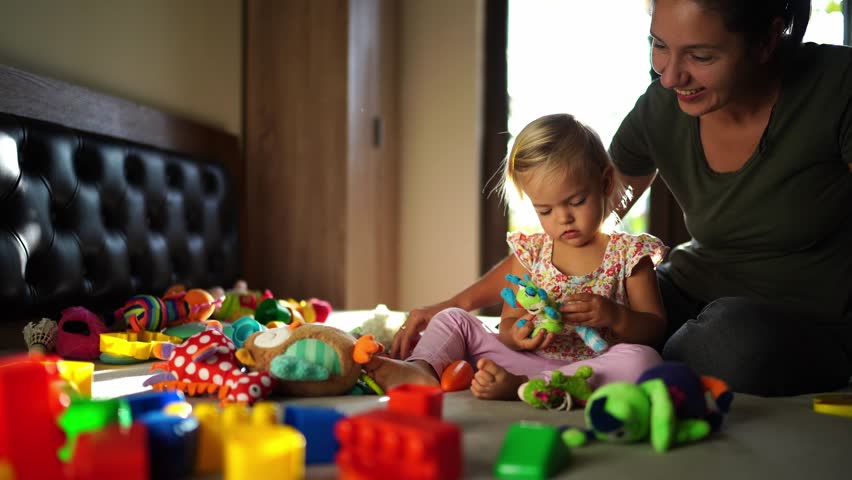 Mom and little girl play with colorful soft toys on the bed