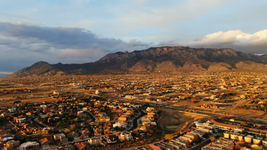 Aerial drone golden sunset toward Sandia Mountains Albuquerque New Mexico with adobe homes pan up