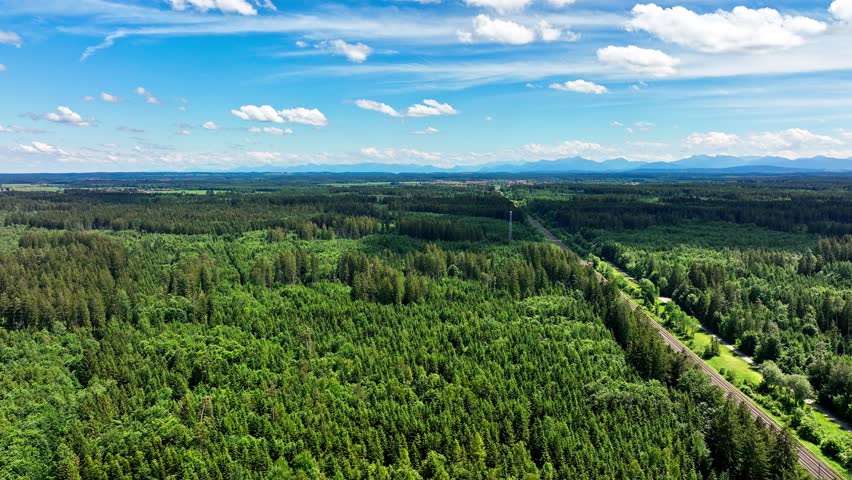 Aerial of a wonderful green forest landscape with a train is coming from the rlower ight side, driving to the horizon in mountain range.
