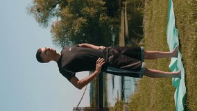 Athletic man doing gymnastics exercises in the morning in park. Vertical video. Healthy lifestyle and workout concept. Man doing stretching exercises in nature. Sport activity