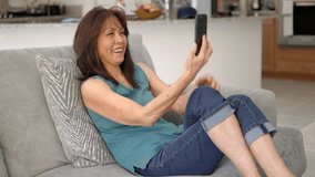 Cheerful attractive woman, nice face, wearing denim jeans smiling laughing using mobile cell phone video chatting looking at family. Middle age asian female using smartphone for internet web cam.